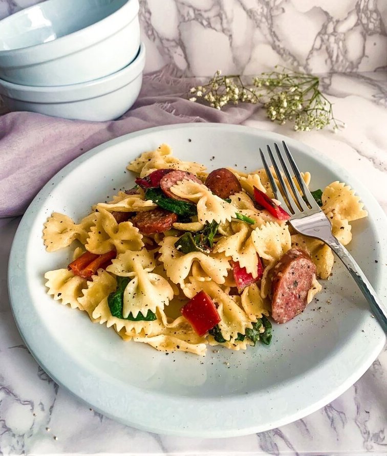 black pepper cream farfalle pasta with sausage and spinach on a marble table