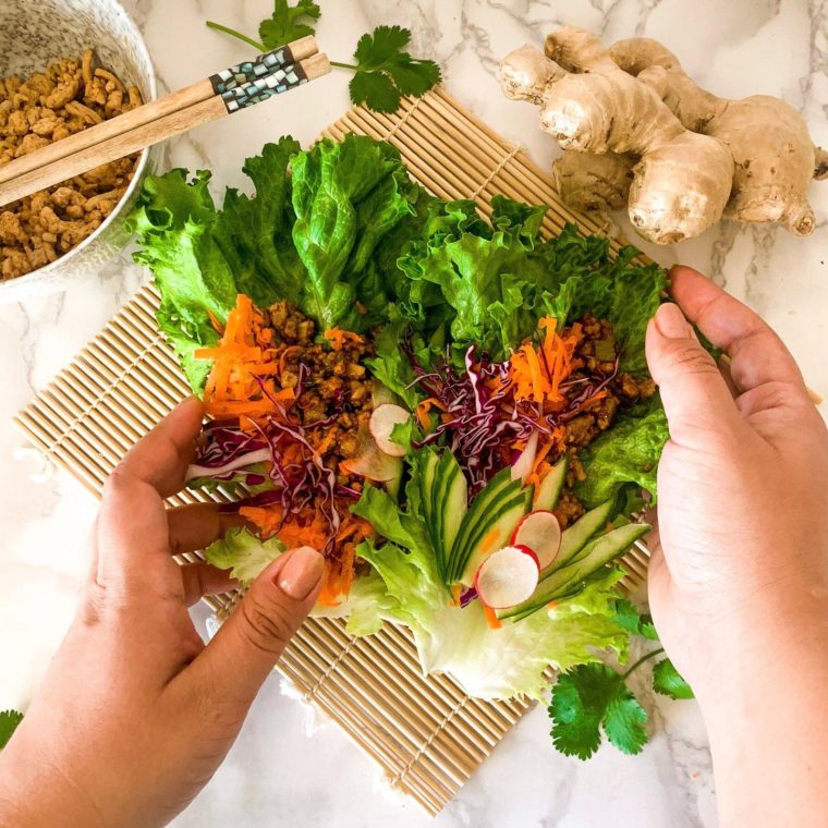 Peanut chicken lettuce wraps with ginger, cucumber and carrots, hands holding both sides